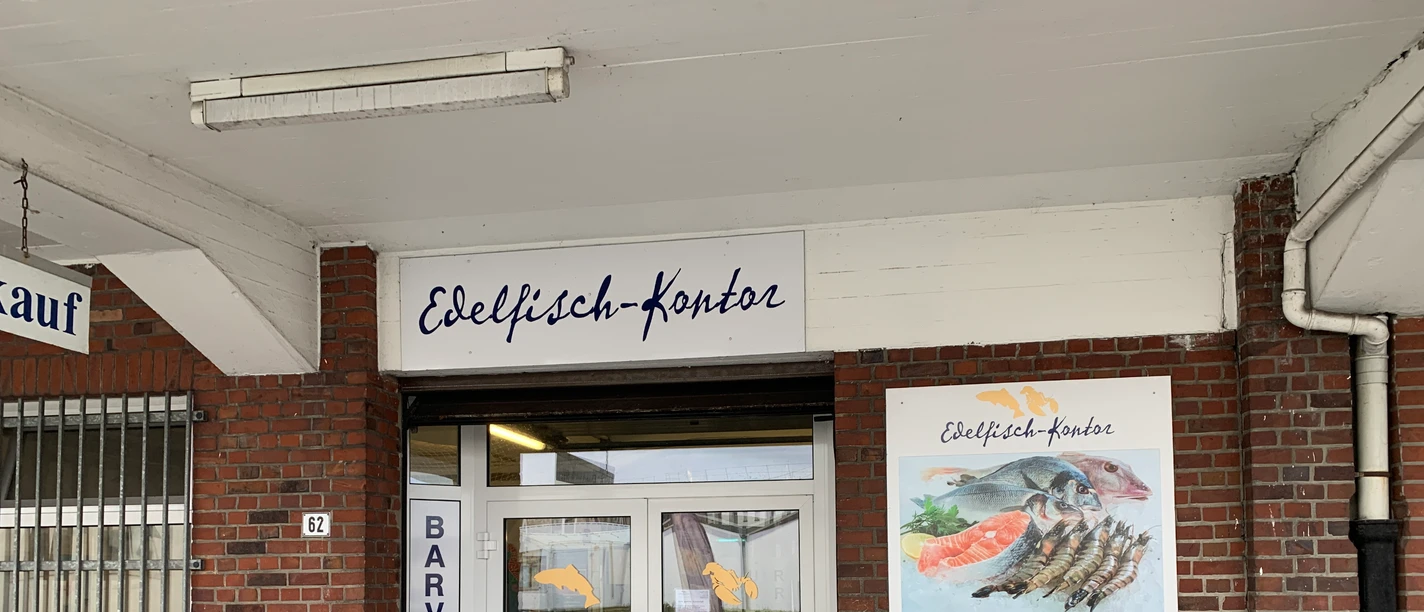 Edelfisch-Kontor IMG_3510 (c) Jasmin Emilia Meyer_Erlebnis Bremerhaven.JPG Eingangsbereich des Edelfisch-Kontors mit Backsteinfassade, Glastüren und Schildern.