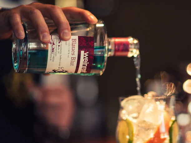Einschenken von blauem Gin aus einer Flasche in ein Glas mit Eis und Zitrone.