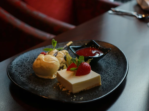 Dessert auf schwarzem Teller: helles Küchlein mit Erdbeeren, Vanilleeis und roter Soße.