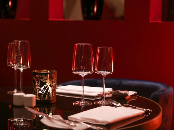 Zwei zu zweit im Restaurant Weinrot (c) Emina_Seiffert.jpg Elegant gedeckter Tisch für zwei Personen mit Weingläsern und Kerzenlicht vor roter Wand.