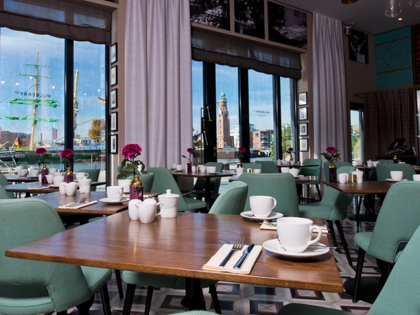MICE Restaurant Mulberry Nord (c) Enno Friedrich.jpg Elegantes Restaurant mit grünen Sesseln und Hafenblick auf ein großes Segelschiff.