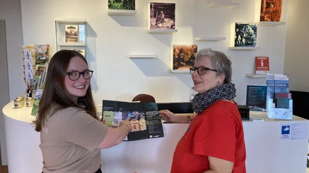 Deux employées se tiennent au front-desk de l'office de tourisme avec des brochures.