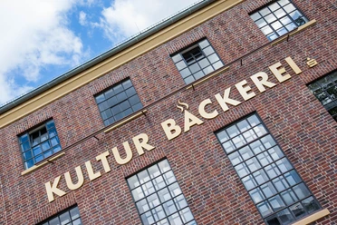 Kulturbäckerei Backsteinfassade mit großen Sprossenfenstern und dem großen Schriftzug Kultur Bäckerei.