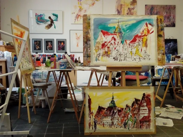 Atelier 6 - Gudrun Jakubeit Helles Atelier mit bunten Stadtlandschaften auf Staffeleien und Malutensilien im Atelier von Gudrun Jakubeit.