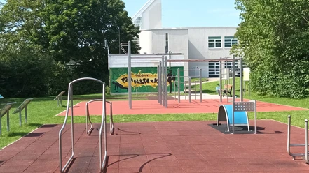 LIONS Fitnesspark Salzgitter: Outdoor-Sportgeräte auf rotem Fallschutzboden im Grünen.