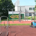 LIONS Fitnesspark Salzgitter: Outdoor-Sportgeräte auf rotem Fallschutzboden im Grünen.