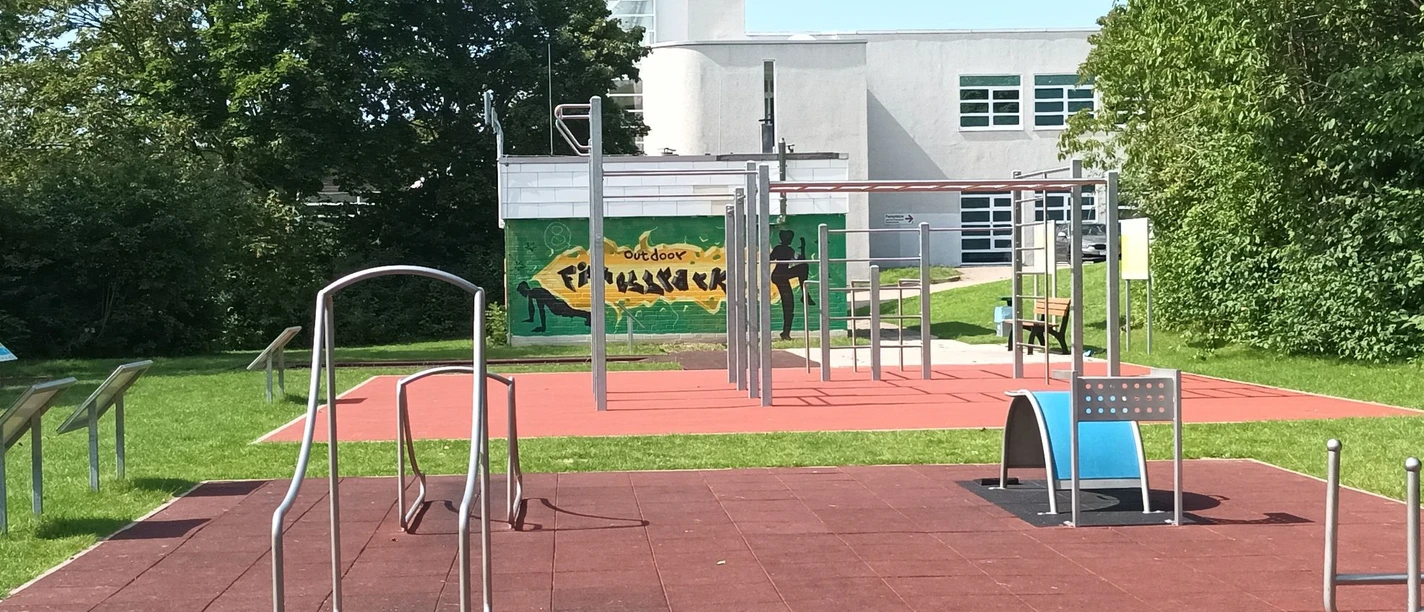 LIONS Fitnesspark Salzgitter: Outdoor-Sportgeräte auf rotem Fallschutzboden im Grünen.
