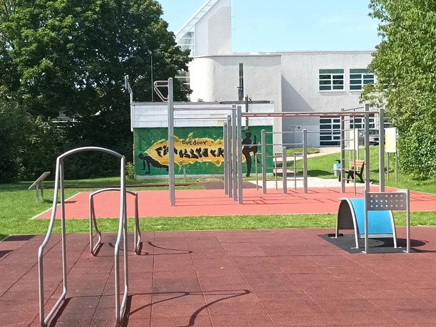 LIONS Fitnesspark Salzgitter: Outdoor-Sportgeräte auf rotem Fallschutzboden im Grünen.