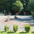 Fitnessgeraete_Gebhardshagen_Minigolfplatz_HD_16zu9.jpg Verschiedene Outdoor-Fitnessgeräte auf einem von Bäumen umgebenen Platz.