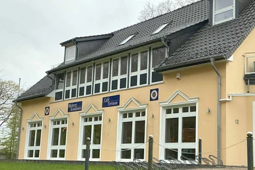 Café in Stendorf Außenansicht eines hellgelben Gebäudes mit großen weißen Fenstern und Schildern für Bäckerei und Café.