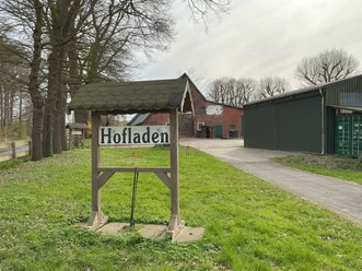Hofladen in Stendorf Holzschild mit der Aufschrift Hofladen an einer Hofeinfahrt vor einem roten Backsteingebäude.