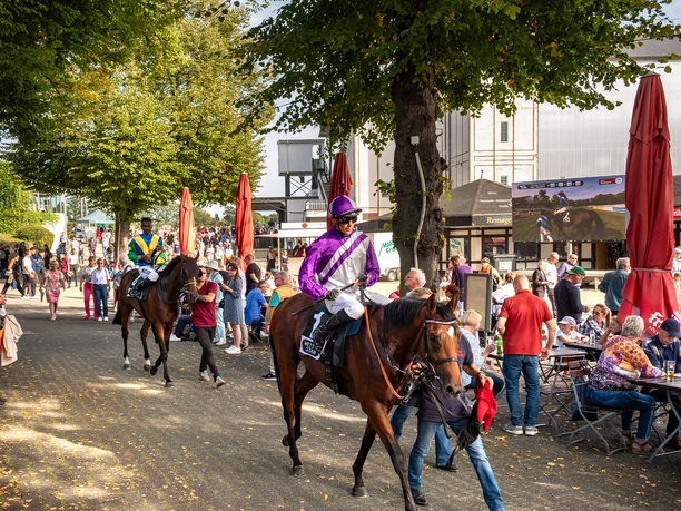 Cologne-Weidenpesch racecourse Riders on racehorses pass through a lively avenue full of visitors on race day