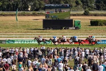 Cologne-Weidenpesch racecourse Horse race in front of a large crowd with four gallopers and video wall in the background