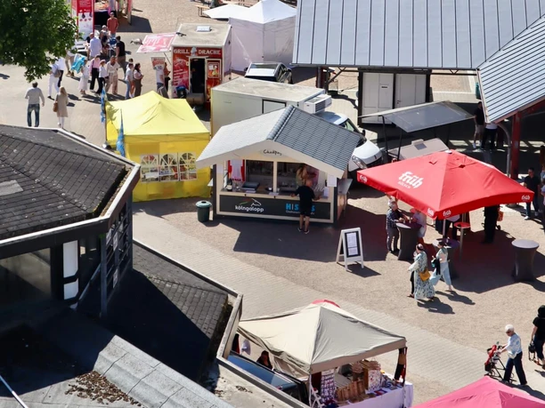 Fisch- und Genussmarkt auf der Rennbahn Köln Weidenpesch Blick auf bunten Open-Air-Markt mit Ständen, Besuchern und großen Bäumen im Hintergrund.
