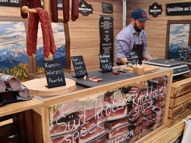 Fisch- und Genussmarkt auf der Rennbahn Köln Weidenpesch Marktstand mit Südtiroler Speck, Kaminwurzen und Verkäufer hinter Holzauslage.