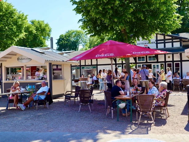 Fish and gourmet market at the Cologne Weidenpesch racecourse People sit at tables in front of a potato pancake stand in a sunny outdoor area.