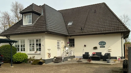 Pension Marianne Weiße Pension mit dunklem Ziegeldach, Eingangstreppe und gepflastertem Vorplatz.
