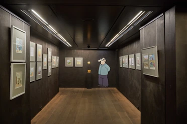 Caricatura Museum Frankfurt - Ausstellung Ausstellungsraum mit gerahmten Comics und Figur an der Wand