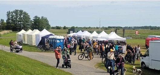 Kunsthandwerkermarkt Greetsiel Besucher spazieren zwischen weißen Zelten auf dem sonnigen Kunsthandwerkermarkt im Grünen.