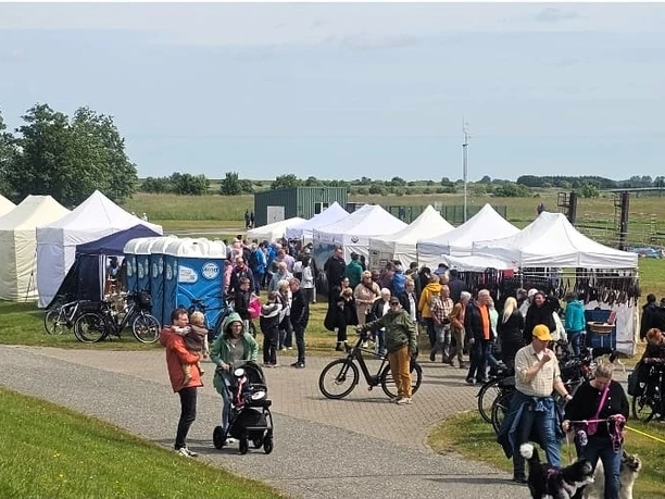Kunsthandwerkermarkt Greetsiel Besucher spazieren zwischen weißen Zelten auf dem sonnigen Kunsthandwerkermarkt im Grünen.