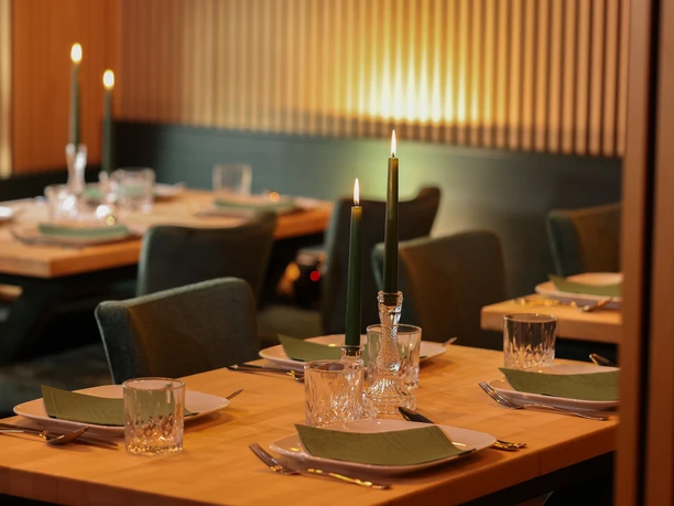 Omagerichte, gedeckter Tisch Eingedeckte Holztische mit grünen Kerzen und Glasgeschirr in einem warm beleuchteten Restaurant