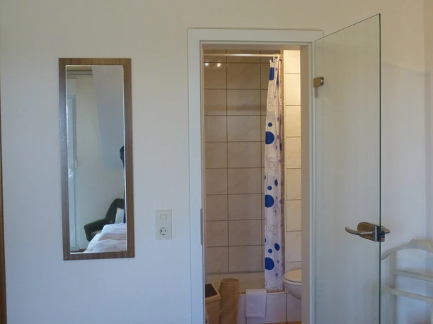 Blick vom Gästezimmer ins Bad mit Dusche, WC und hellen Fliesen