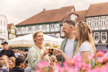 Weinmarkt Celle – Ein Glas Wein in sommerlicher Atmosphäre in Drei Freunde stoßen mit Weißwein auf dem Weinmarkt in Celle an und genießen das sommerliche Ambiente zwischen historischen Fachwerkhäusern der Altstadt.