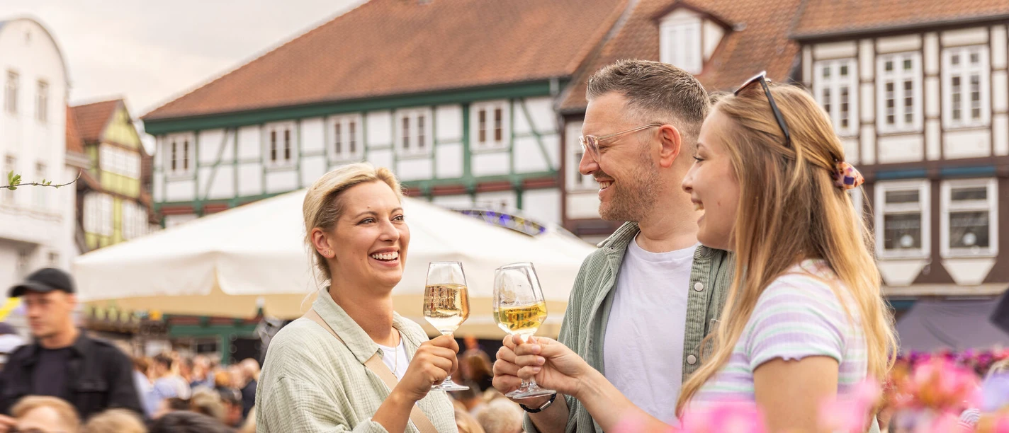 Weinmarkt Celle – Ein Glas Wein in sommerlicher Atmosphäre in Drei Freunde stoßen mit Weißwein auf dem Weinmarkt in Celle an und genießen das sommerliche Ambiente zwischen historischen Fachwerkhäusern der Altstadt.