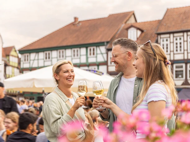 Weinmarkt Celle – Ein Glas Wein in sommerlicher Atmosphäre in Drei Freunde stoßen mit Weißwein auf dem Weinmarkt in Celle an und genießen das sommerliche Ambiente zwischen historischen Fachwerkhäusern der Altstadt.