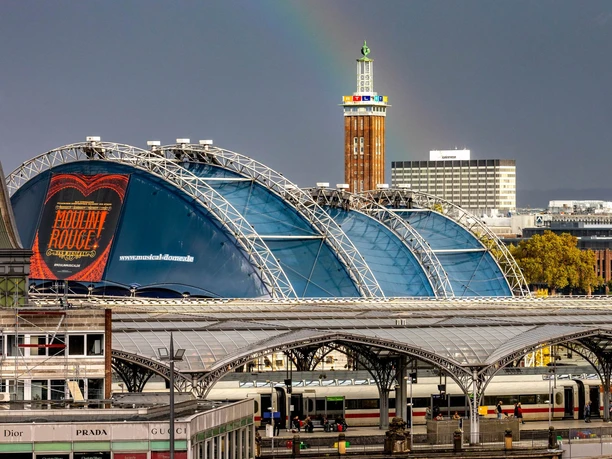 Musical Dome Blick auf den Musical Dome in Köln mit blauem Dach und Regenbogen über dem Bahnhofsumfeld