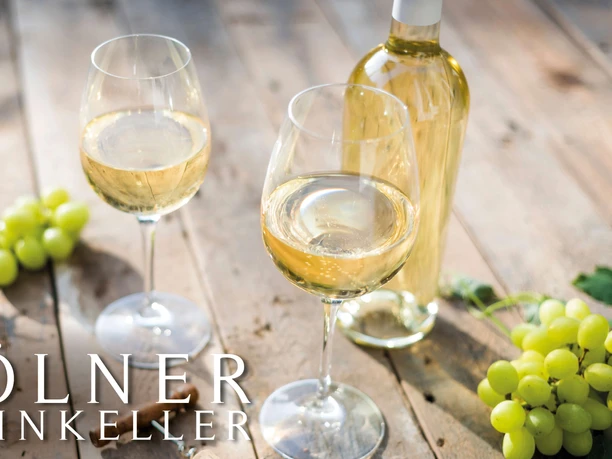 Stand-up tasting in the Cologne wine cellar - white wine Two glasses of white wine with bottle and light grapes arranged on a wooden table.