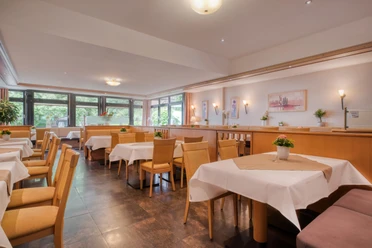 Heller Restaurantbereich mit gedeckten Tischen, Holzstühlen und großen Fenstern.