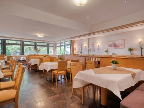 Heller Restaurantbereich mit gedeckten Tischen, Holzstühlen und großen Fenstern.