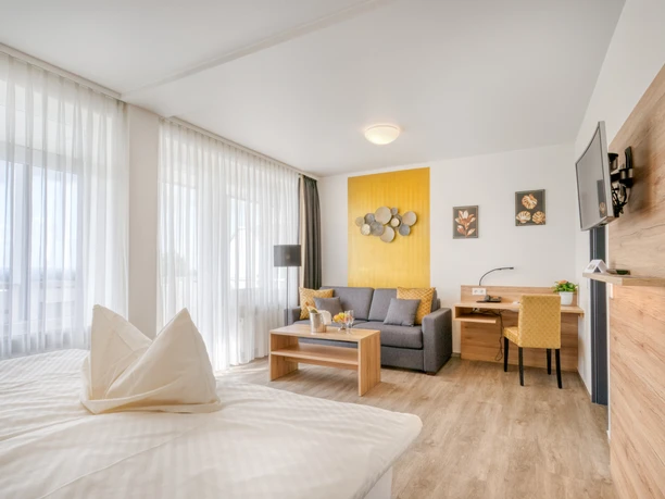 Wiehen Therme Suite Helle Suite mit Doppelbett, Sofa, Schreibtisch und großem Fenster mit Vorhängen