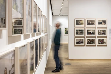 The Photographic Collection/SK Stiftung Kultur Exhibition room with many framed photographs and a blurred person looking at them