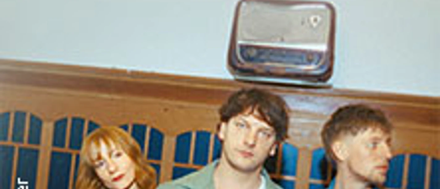 Drei Personen vor einer Holzwand, oben ein Radio und der Schriftzug Naked Cameo