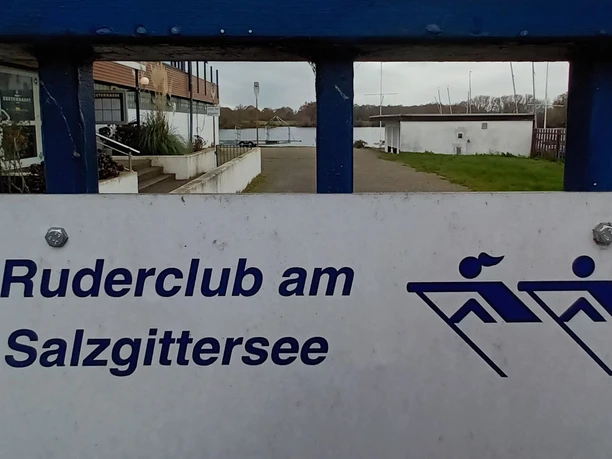 Ruderclub am Salzgittersee_HD_16zu9.jpg Schild mit Aufschrift Ruderclub am Salzgittersee und Logo, im Hintergrund der Weg zum Wasser.