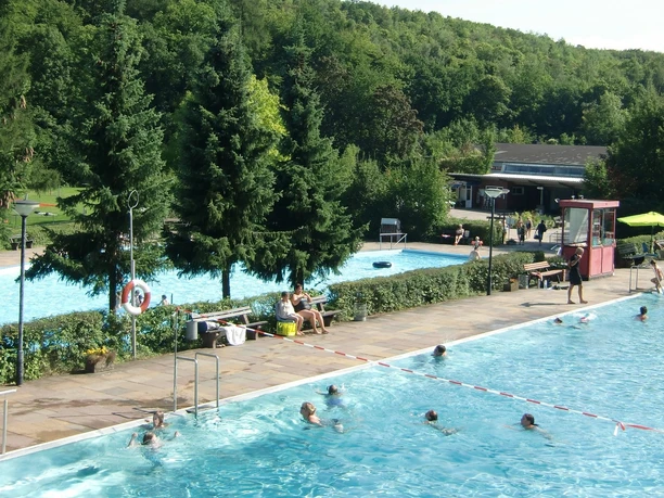 Waldschwimmbad_Salzgitter-Gebhardshagen_HD_16zu9.jpg Freibad am Waldrand mit schwimmenden Gästen in zwei blauen Becken und großen Nadelbäumen.