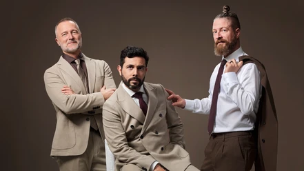 Drei Sänger der Italian Tenors in eleganten Anzügen vor dunklem Studiohintergrund.