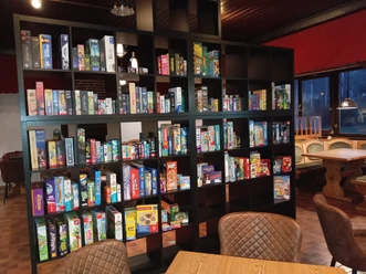 Spielcafe Knaus Campingpark Wingst Einladendes Spielcafé mit einem großen Regal voller bunter Brettspiele und Sitzgelegenheiten.