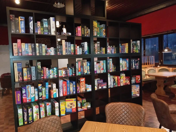 Spielcafe Knaus Campingpark Wingst Einladendes Spielcafé mit einem großen Regal voller bunter Brettspiele und Sitzgelegenheiten.