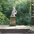 Schlosspark Dittersbach Skulptur der Diana Figur mit einem Hirsch auf einem Sockel, umgeben von Bäumen und Natur.