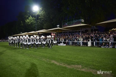 Advendo Sneek beim Finale (Mittel) Eine uniformierte Marching Band marschiert nachts bei Flutlicht auf Rasen vor einem Publikum.