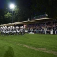Advendo Sneek beim Finale (Mittel) Eine uniformierte Marching Band marschiert nachts bei Flutlicht auf Rasen vor einem Publikum.
