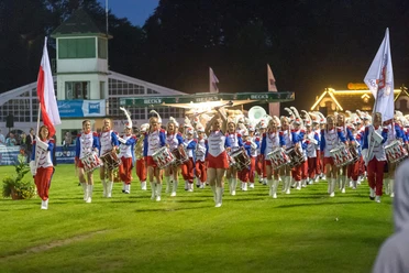 Orkiestra Grandioso Radom Polen Ein Orchester in rot-weißen Uniformen marschiert mit Fahnen nachts über den Rasen.