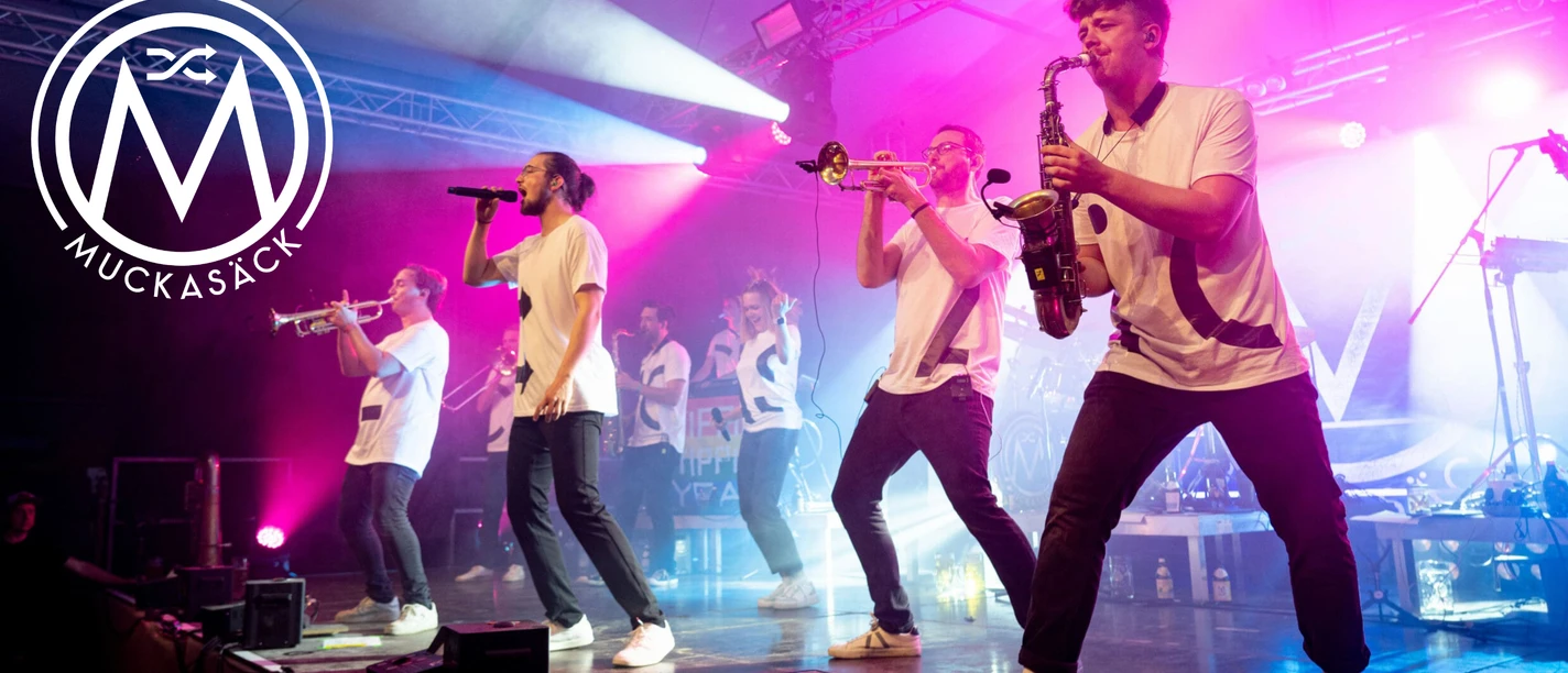 Muckasäck EMC Die Band Muckasäck spielt live auf einer pink beleuchteten Bühne mit Blasinstrumenten und Gesang.