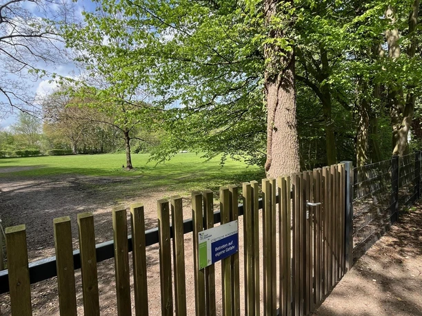 Hundewiese Stadtpark Botanischer Garten Holzzaun vor weiter Wiese mit großen Bäumen im Botanischen Garten Gütersloh