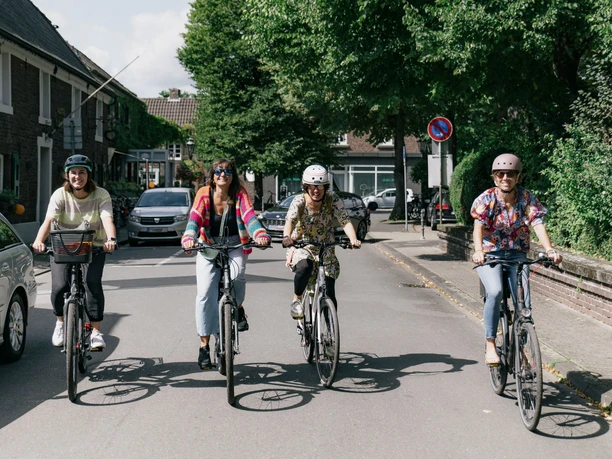 Vier Erwachsene fahren auf Fahrrädern durch einen urbanen Raum.