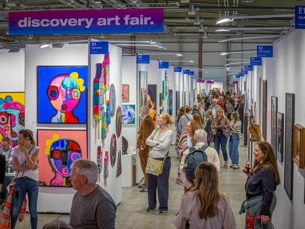 Discovery Art Fair Cologne People view colorful modern art in a busy exhibition hall at the art fair