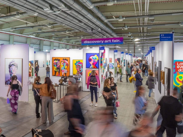 Discovery Art Fair Cologne Lively art fair hall with colorful paintings and groups of visitors between the stands